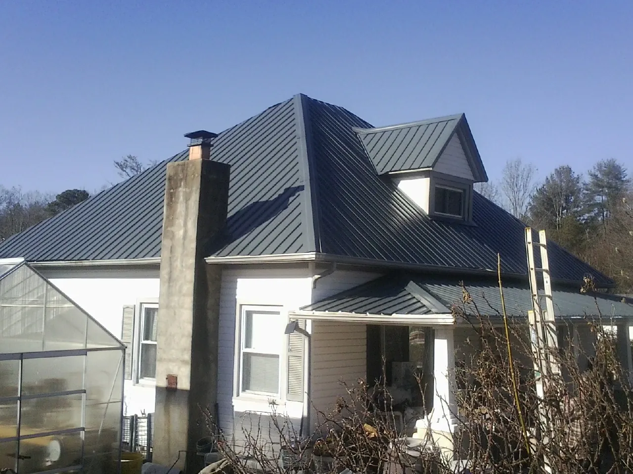 Dark blue standing seam metal roof on a white farmhouse with dormer in Houlton