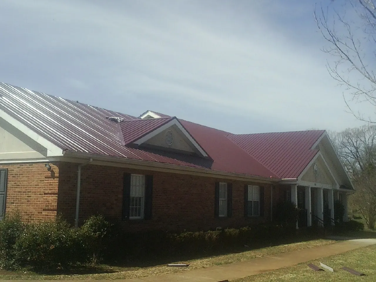 Red metal roof with gabled entries on a long brick building, from a Hail Damage Roof Repair job in Houlton