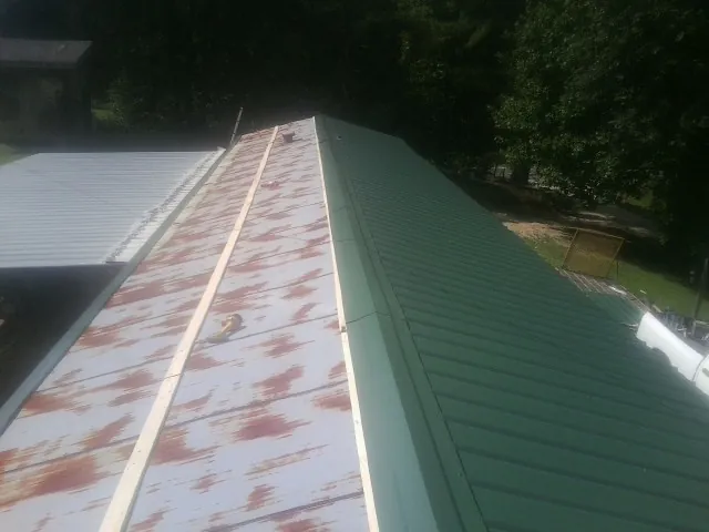 Old rusted panels beside newly installed green metal roofing — Wind Damage Roof Repair by Roofing Brothers in Houlton
