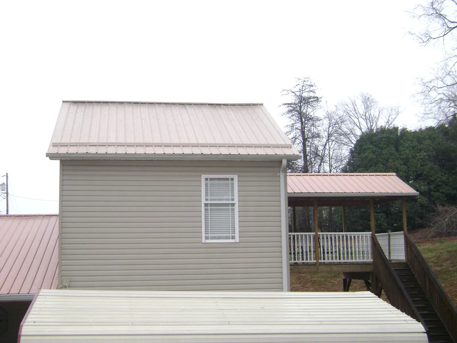 Tan metal roofs on a two story addition and attached porch, from a Roof Replacement job in Houlton